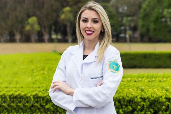 Suelen Szymanski, fotógrafa da Petit Poá Fotografia e fotógrafa voluntária da DEBRA Brasil, olhando para a câmera vestindo um jaleco de enfermeira 