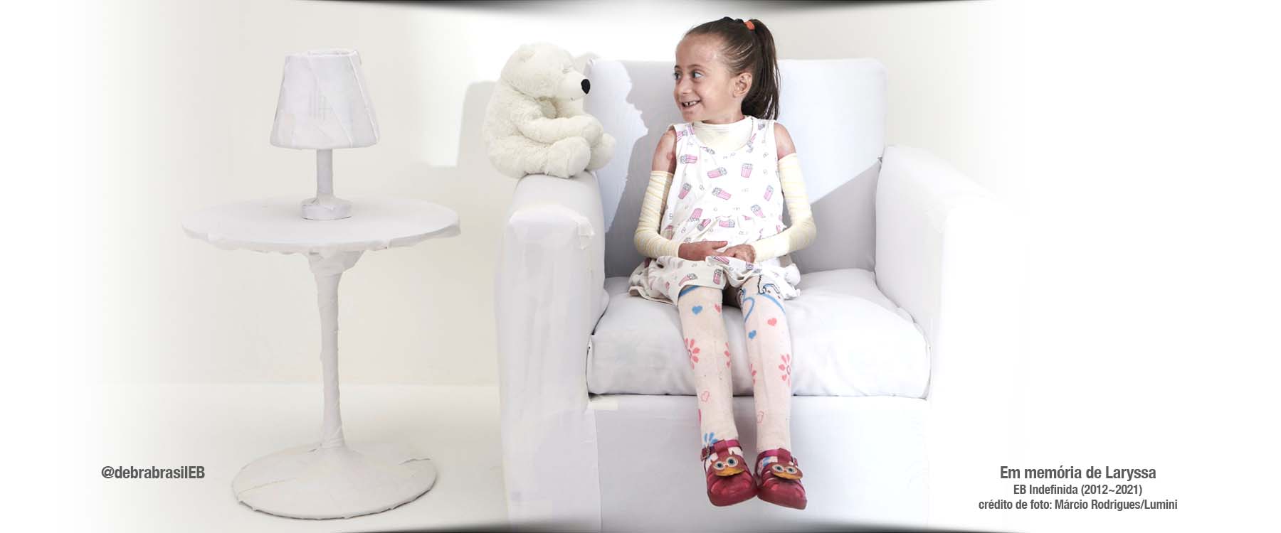 A Laryssa, menina com epidermólise bolhosa (EB) indefinida, com um sorriso maroto olhando com curiosidade um ursinho de pelúcia
