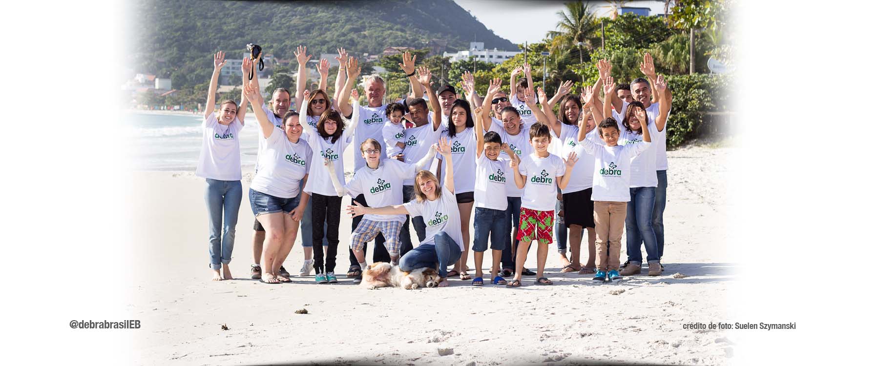 Voluntários, pessoas com epidermólise bolhosa (EB) e seus familiares em um grupo de mais de 20 pessoas na praia, vestindo a camiseta da DEBRA