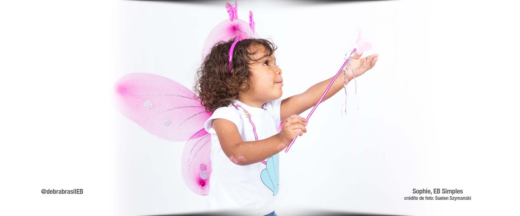 Sophie, menina com epidermólise bolhosa (EB) simples, vestida de fada com asas de borboleta, tiara e varinha de condão