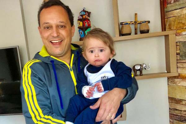 Leandro, presidente da DEBRA Brasil, sorrindo para a câmera enquanto segura no colo o sobrinho Theo, bebê que nasceu com epidermólise bolhosa (EB) e foi o motivo principal do seu envolvimento com a causa