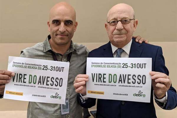 Renato Lombardi, apresentador do Balanço Geral, e Adriano, funcionário da Record TV, segurando o banner da campanha Vire do Avesso, de conscientização da epidermólise bolhosa (EB)