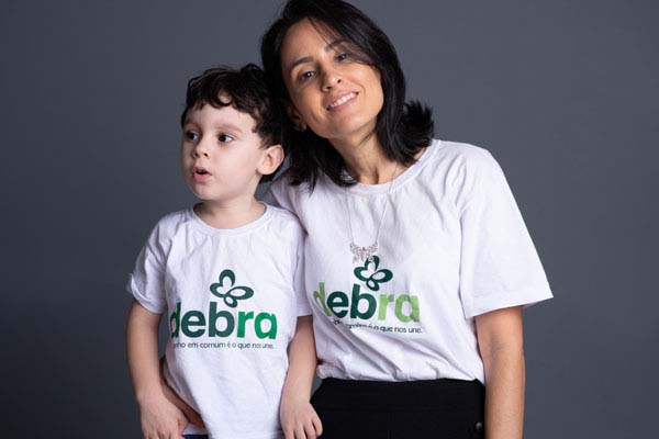 Dra. Rosalie Torrelio e o filho vestem a camiseta da DEBRA. Ela é voluntária e apresentadora do DEBRA Talks, um programa de entrevistas sobre a epidermólise bolhosa (EB) com profissionais e a comunidade EB 
