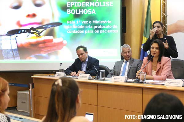 O presidente da DEBRA fazendo anotações, enquanto a primeira-dama, Michelle Bolsonaro, fala no microfone no lançamento da consulta pública do PCDT de epidermólise bolhosa (EB)